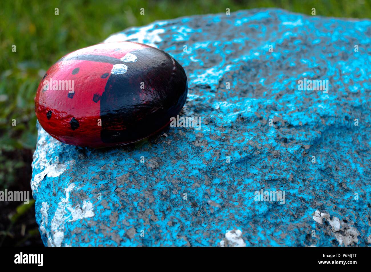 Ein Insekt namens einen Marienkäfer ist der Stein und malte Tinten. Die Figur steht im Garten auf einem blauen Stein. Sehr schöne und interessante h Stockfoto