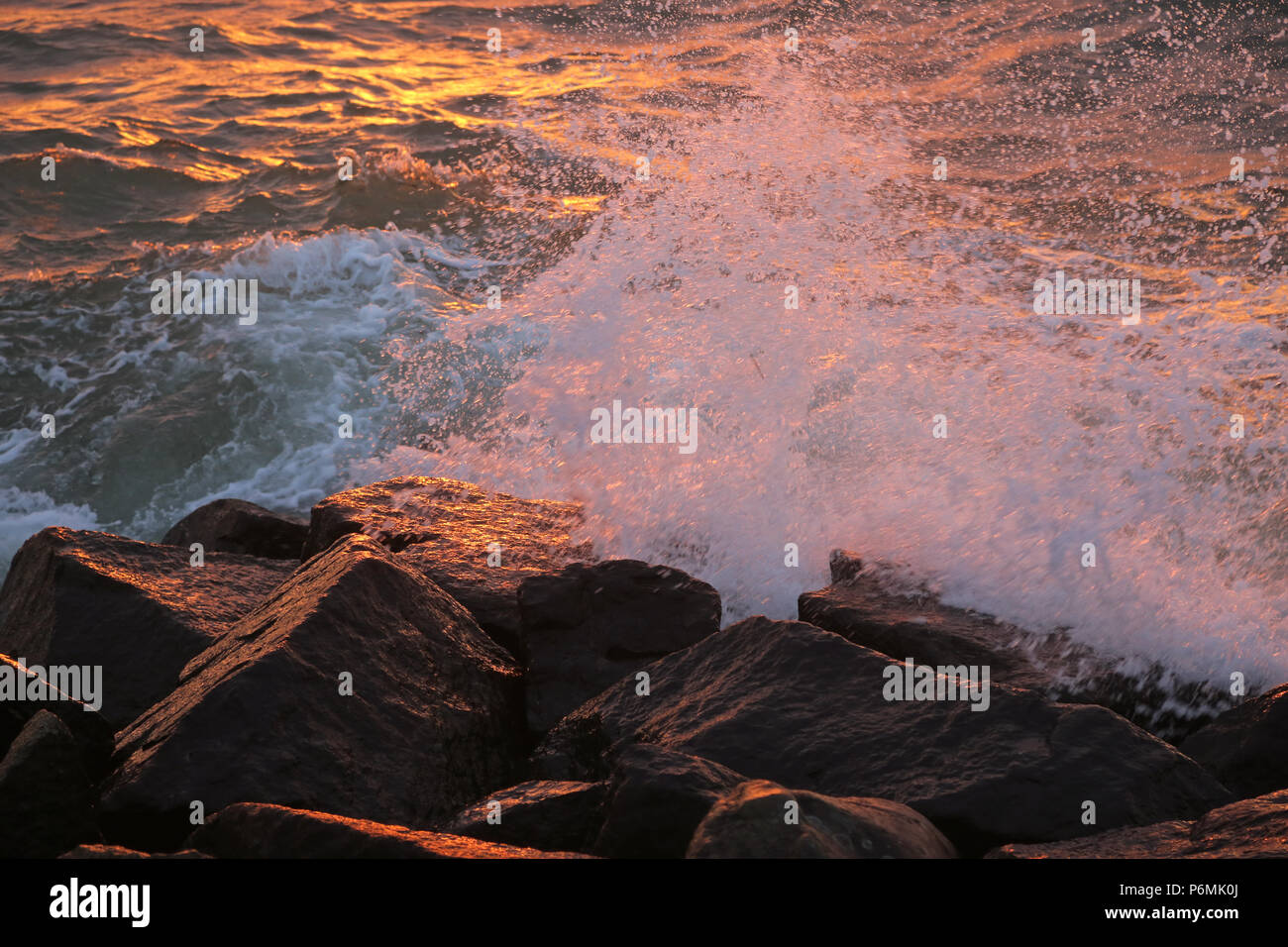 Warnemünde, Wellen im Abendlicht auf Felsen brechen Stockfoto