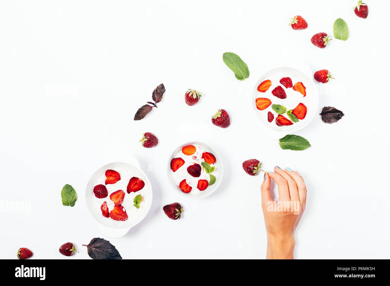 Woman's Hand, denn frische Erdbeere unter den Schalen von Speiseeis auf weißem Hintergrund, Ansicht von oben. Flach Anordnung der Sommer kalte Desserts eingerichtet wi Stockfoto