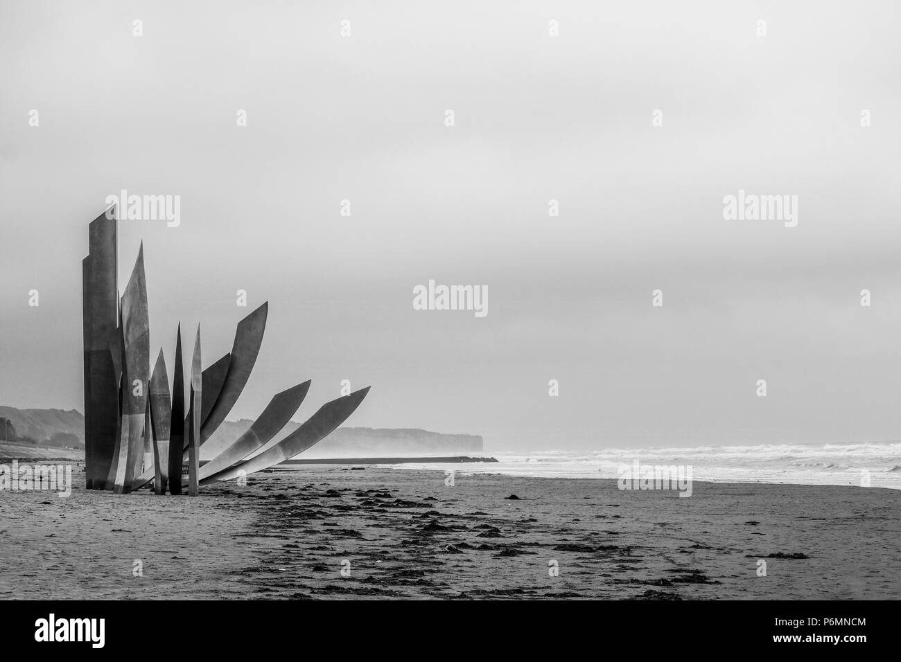 Vierville-sur-Mer, Frankreich. Die Skulptur 'Les Braves' in den Vordergrund der schwarzen und weißen Schoß sitzt, Blick nach Westen auf einer menschenleeren Omaha Beach an einem bewölkten D Tag Geburtstag. Stockfoto