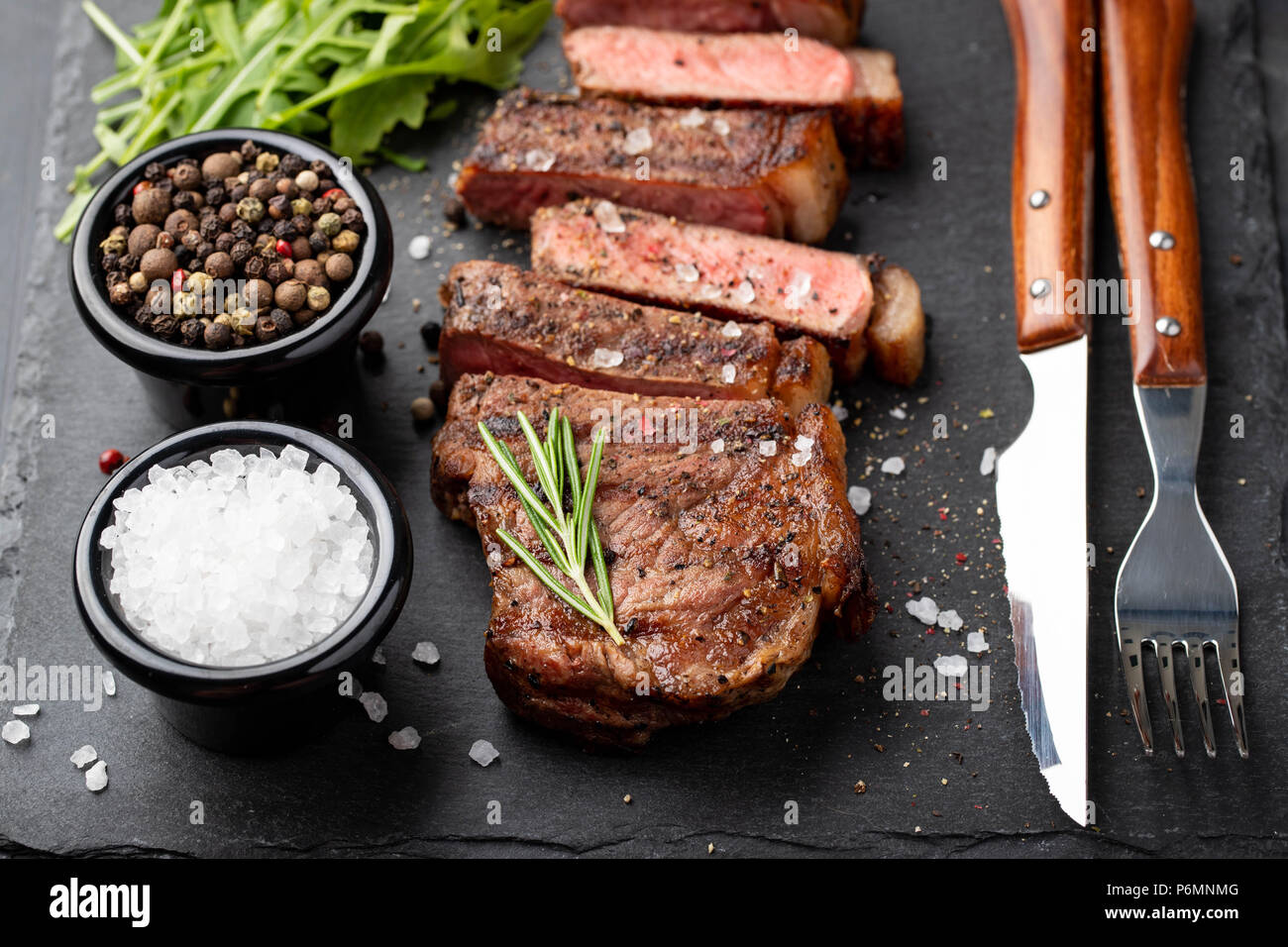 Closeup bereit Steak New York fleischrassen von Black Angus mit Kräutern, Knoblauch und Butter auf einem Stein zu essen. Das fertige Gericht zum Abendessen auf einem dunklen Stein Hintergrund. Ansicht von oben Stockfoto