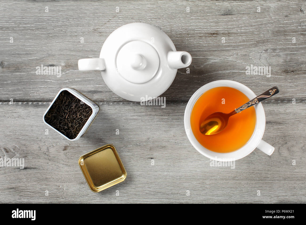 Table Top - Messing Tee Caddy, weißes Porzellan Teekanne und Tasse aus Keramik mit silbernen Löffel und heiße Amber trinken, auf grau Holzschreibtisch. Stockfoto