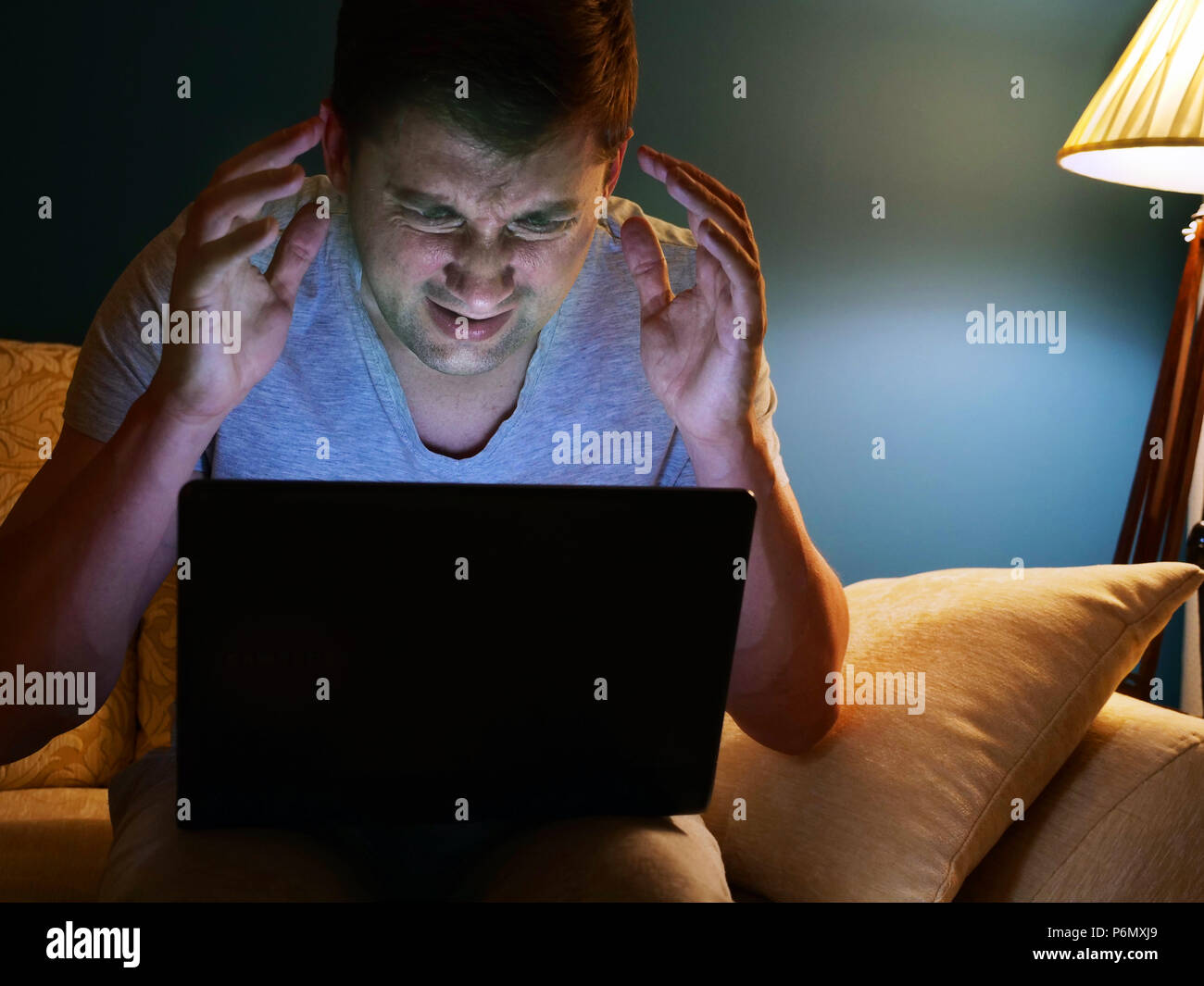 Erschrocken oder wütenden Mann mit Laptop auf einem Sofa. Am Abend Zeit. Stockfoto