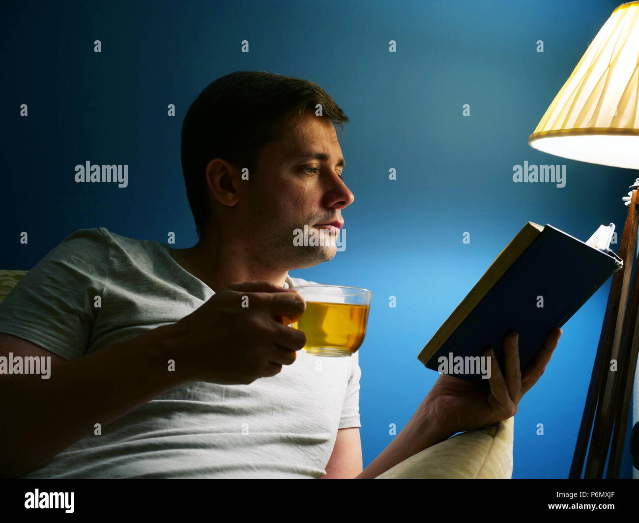 Mann mit Tasse Tee ist das Lesen Buch am Abend. Entspannung. Stockfoto