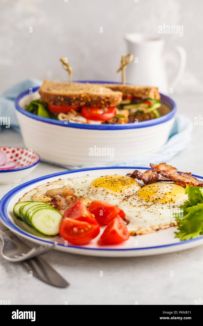 Spiegeleier mit Speck und ein Sandwich mit Fleisch, Käse und Gemüse. Lecker herzhaften Frühstück. Stockfoto