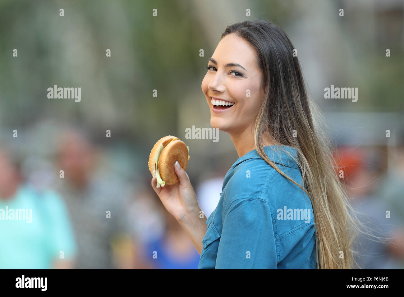 Happy woman holding einen Burger in suchen Sie auf der Straße Stockfoto