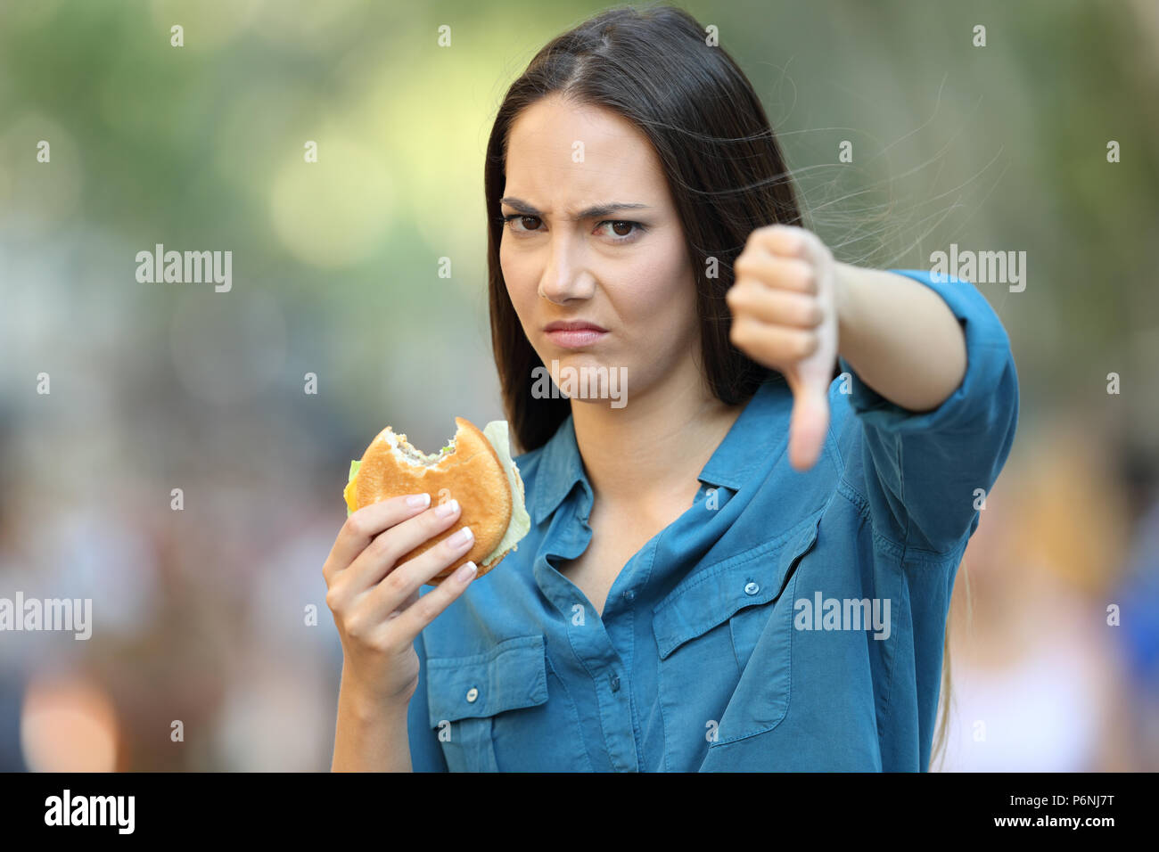 Vorderansicht Portrait von eine wütende Frau ablehnen, einen Burger mit Daumen nach unten auf der Straße Stockfoto