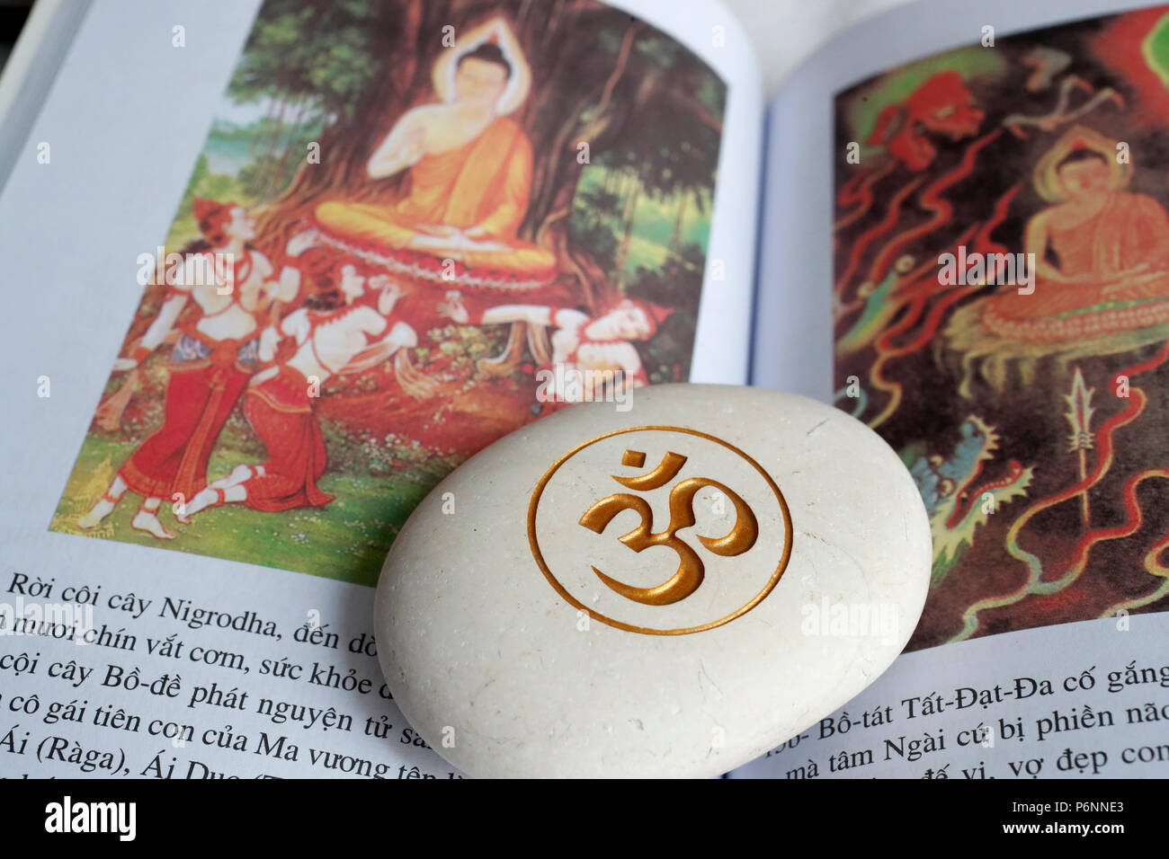 Die Om oder Aum Symbol von Hinduismus und Buddhismus auf einen weissen Stein. Buch über das Leben des Buddha. Stockfoto