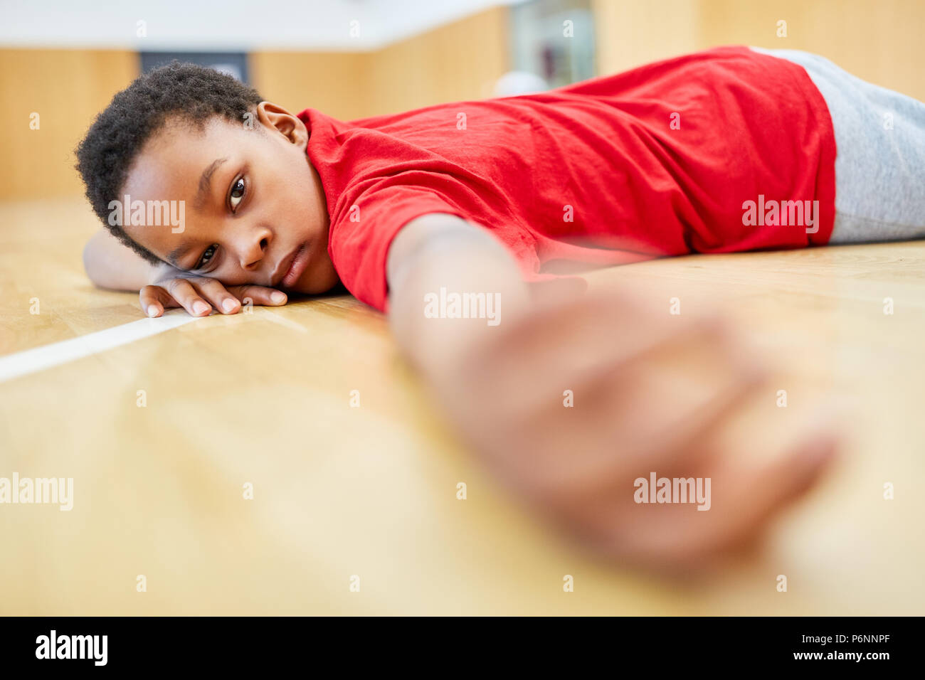 Afrikanischen Jungen liegt in der Turnhalle erschöpft nach dem Sportunterricht Stockfoto