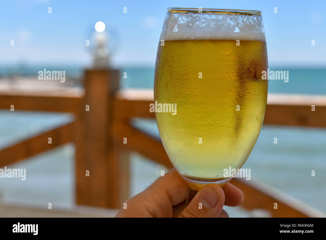 Toast mit einem Verschwitzten Tasse kaltes Bier an einem heissen Sommertag in einem Restaurant am Meer Stockfoto