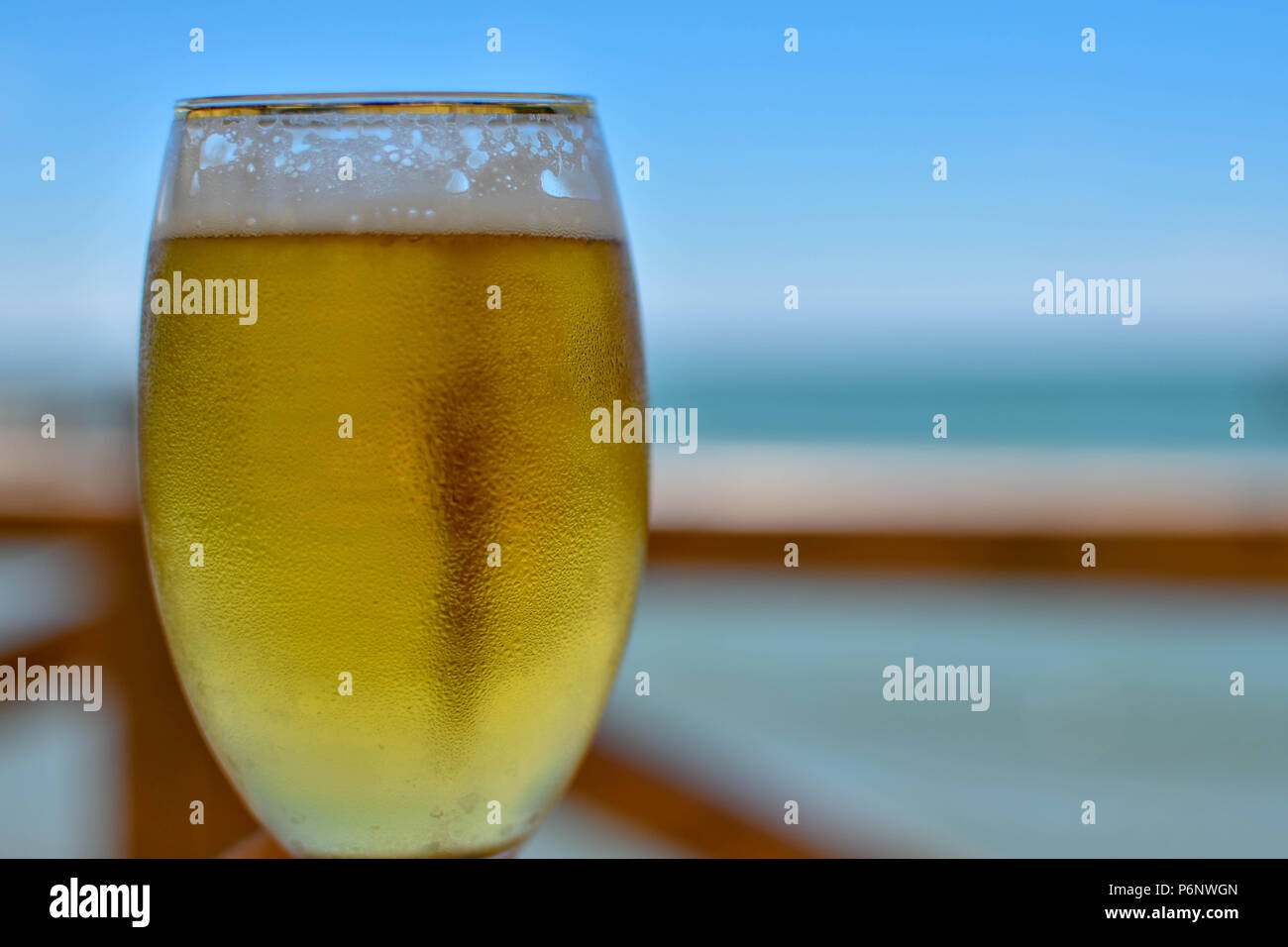 Toast mit einem Verschwitzten Tasse kaltes Bier an einem heissen Sommertag in einem Restaurant am Meer Stockfoto