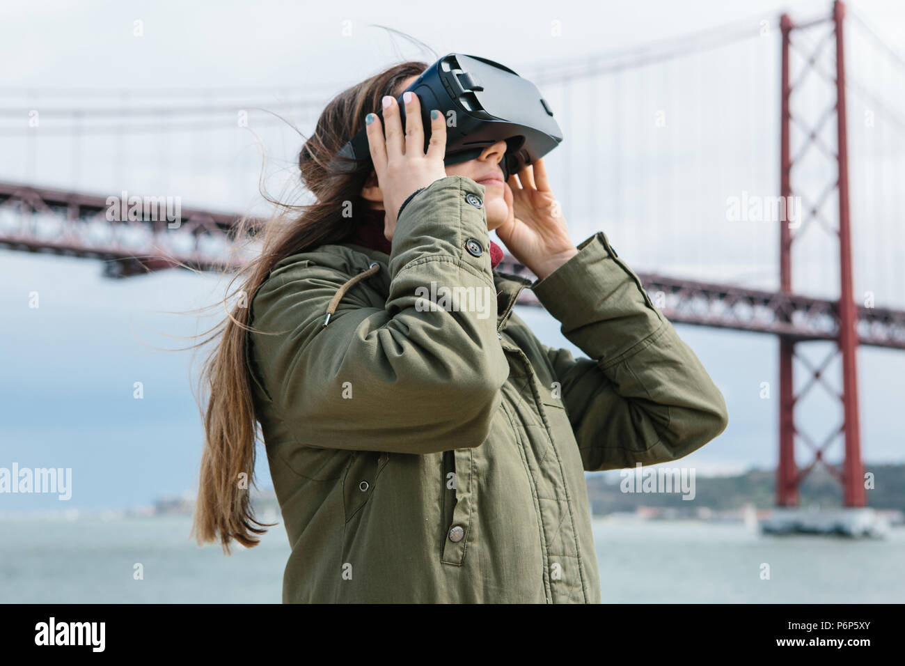 Junge schöne Mädchen mit Virtual reality Brillen. 25 April Brücke in Lissabon im Hintergrund. Das Konzept der modernen Technologien und deren Einsatz im täglichen Leben Stockfoto