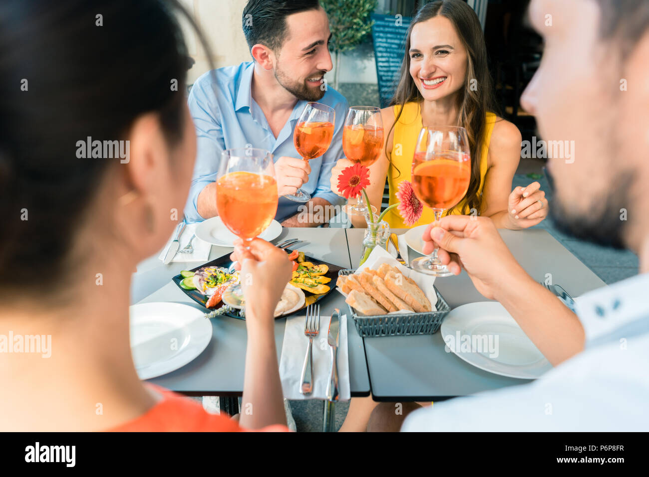 Zwei glückliche junge Paare toasten beim zusammen im Restaurant sitzen Stockfoto