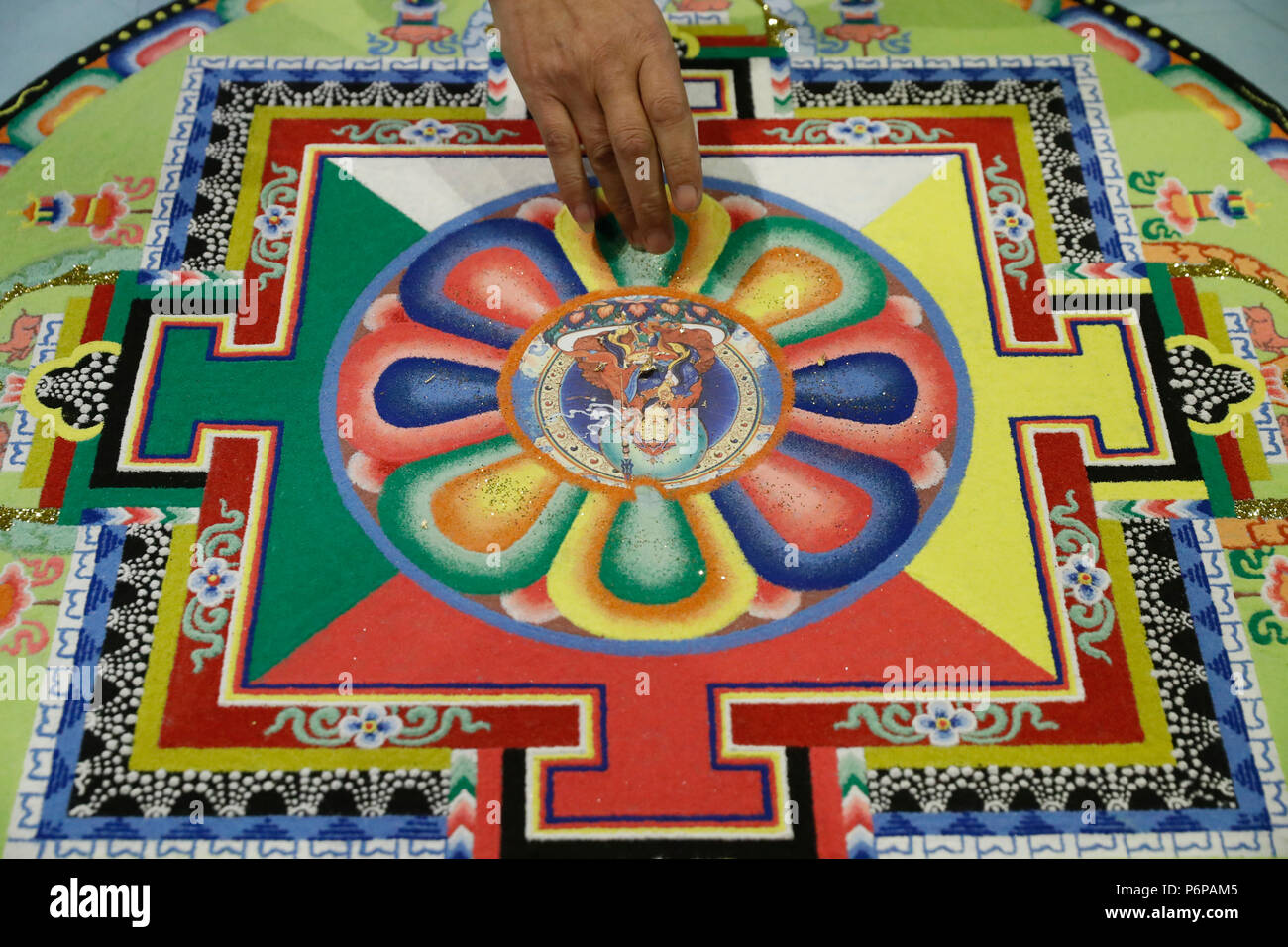 Ein tibetischer Mönch nutzt seine Finger farbige Mischung Sand Mandal und schwenken Sie sie auf einen Haufen. Stockfoto