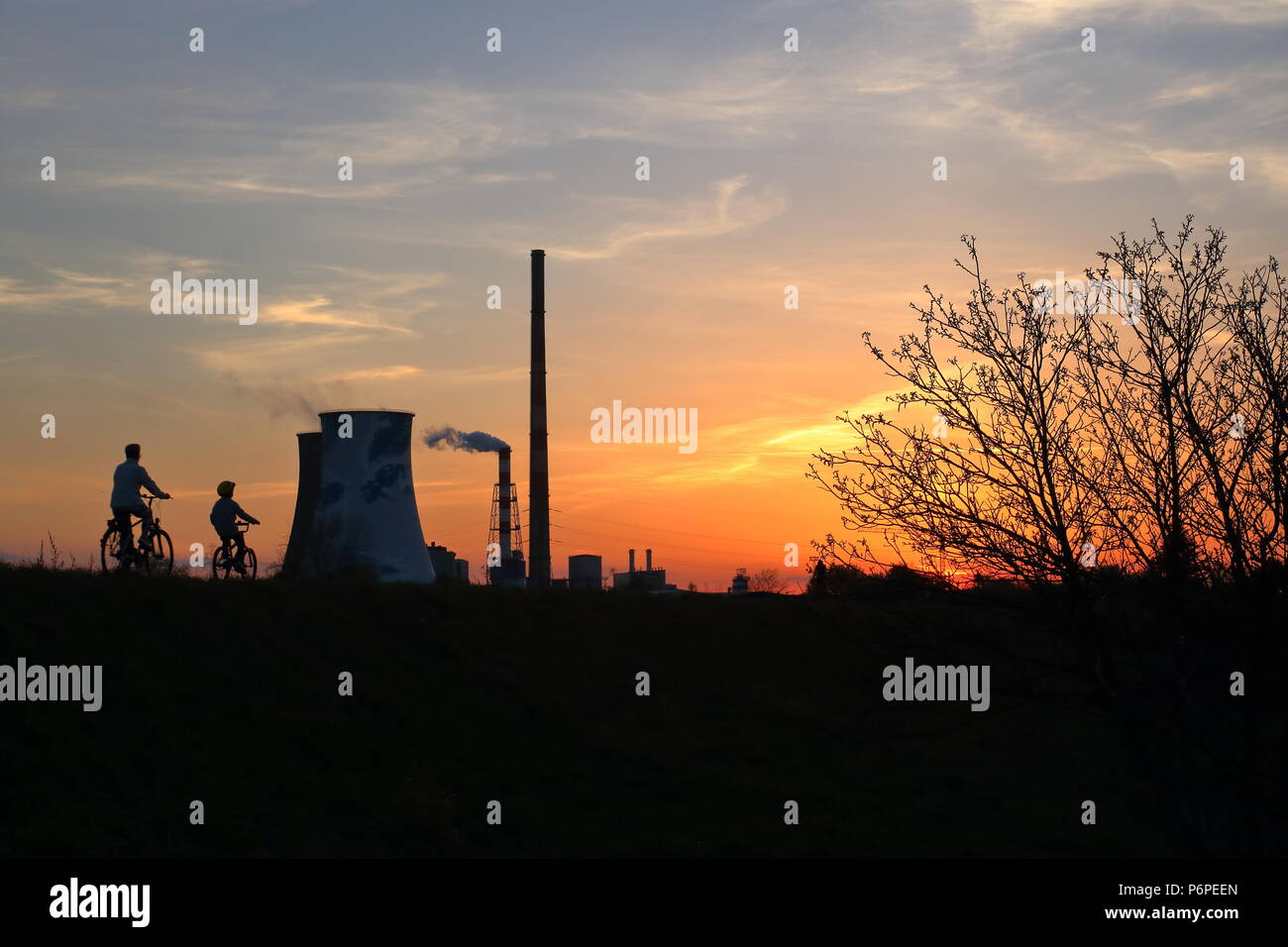 Sonnenuntergang, ornage Sky, in der Dämmerung Baum, Radweg mit zwei Radfahrer, paretna und Kinder, Gruppe von hohen und großen smkoe chimeys, von Ihnen Stockfoto