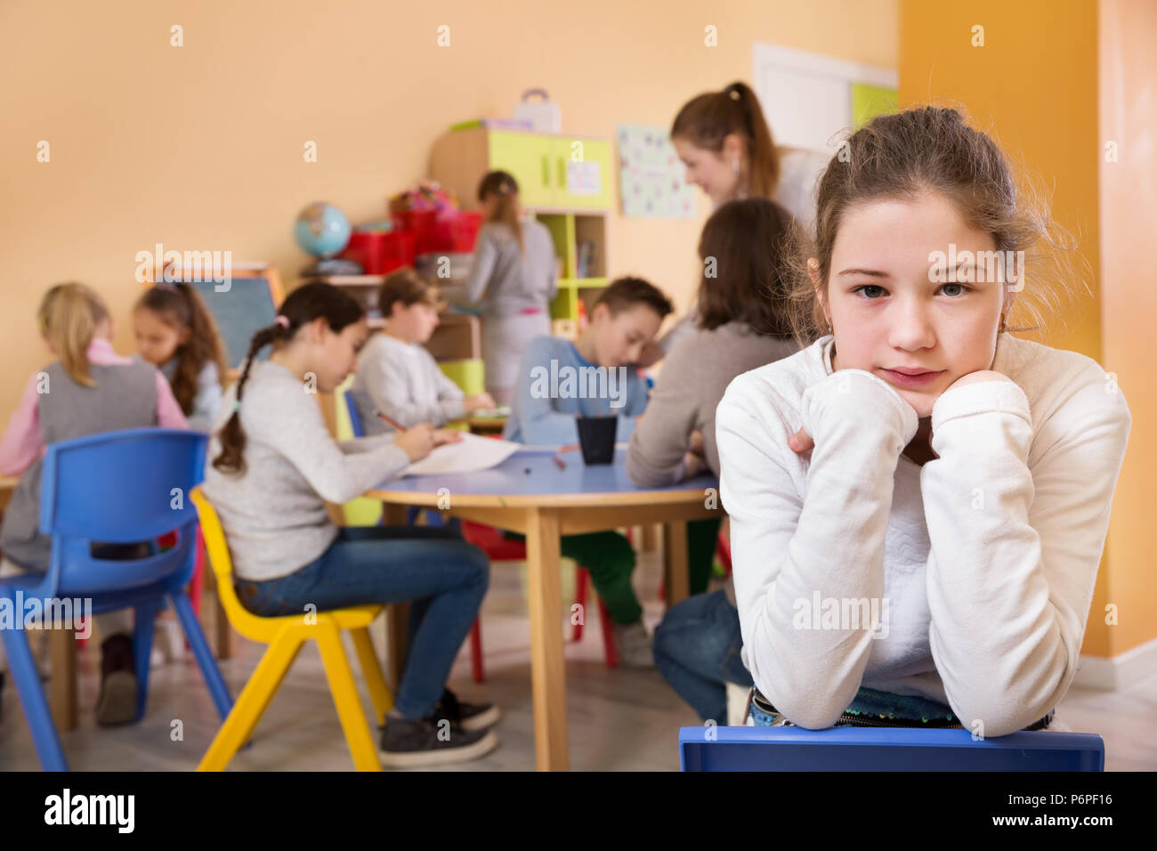 Verärgert stehendes Mädchen in einem Schulzimmer auf Hintergrund mit Schüler studieren mit Lehrer Stockfoto