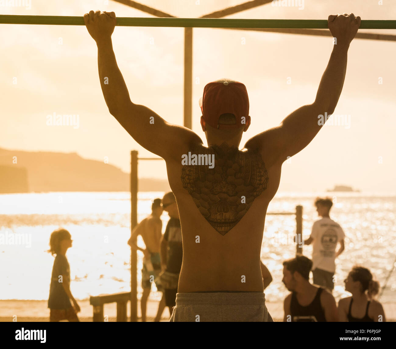 Ansicht der Rückseite des muskulösen Mann mit Zurück tattoo Zug tut ups/Chin ups am Strand in Spanien Stockfoto