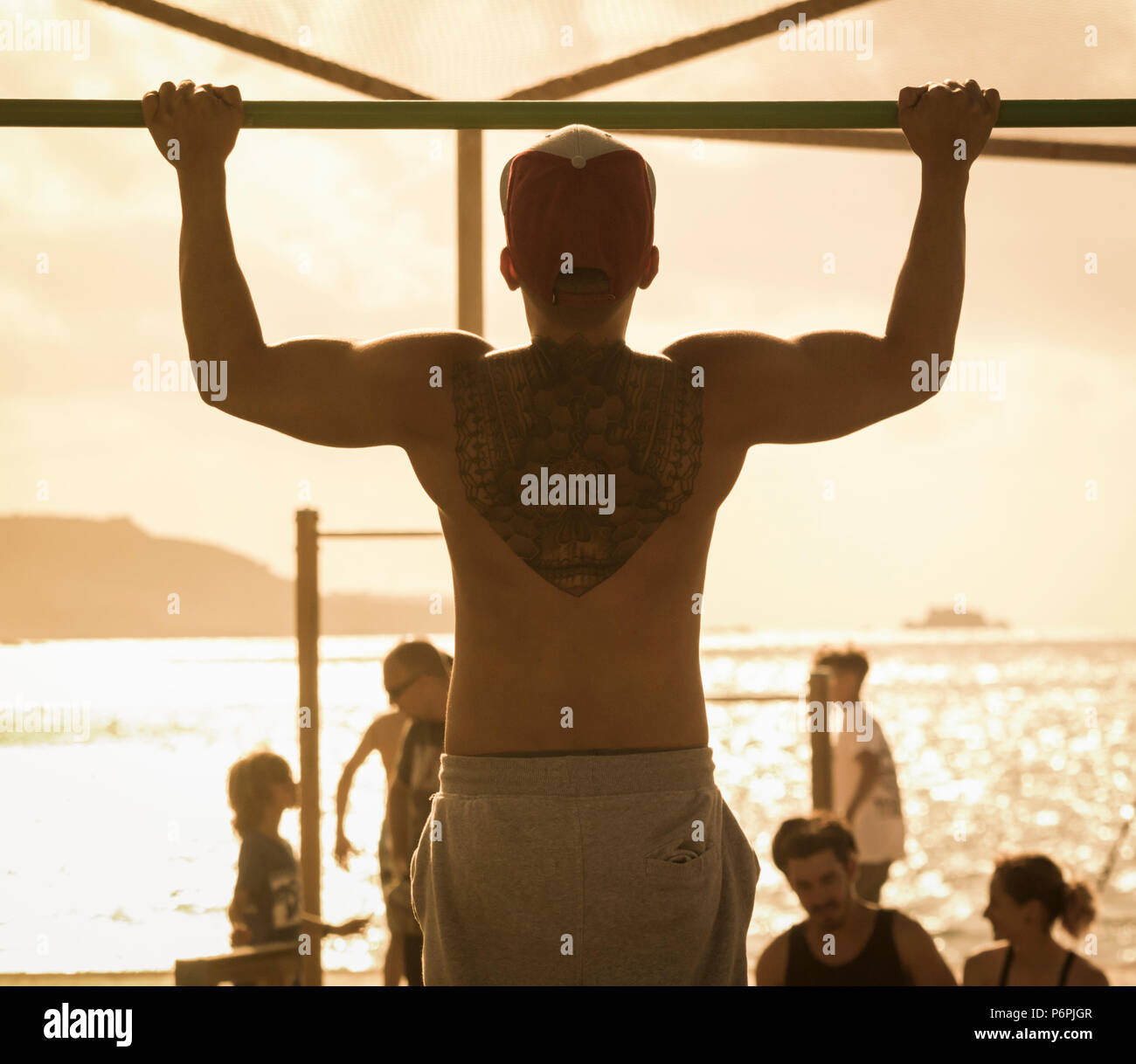 Ansicht der Rückseite des muskulösen Mann mit Zurück tattoo Zug tut ups/Chin ups am Strand in Spanien Stockfoto