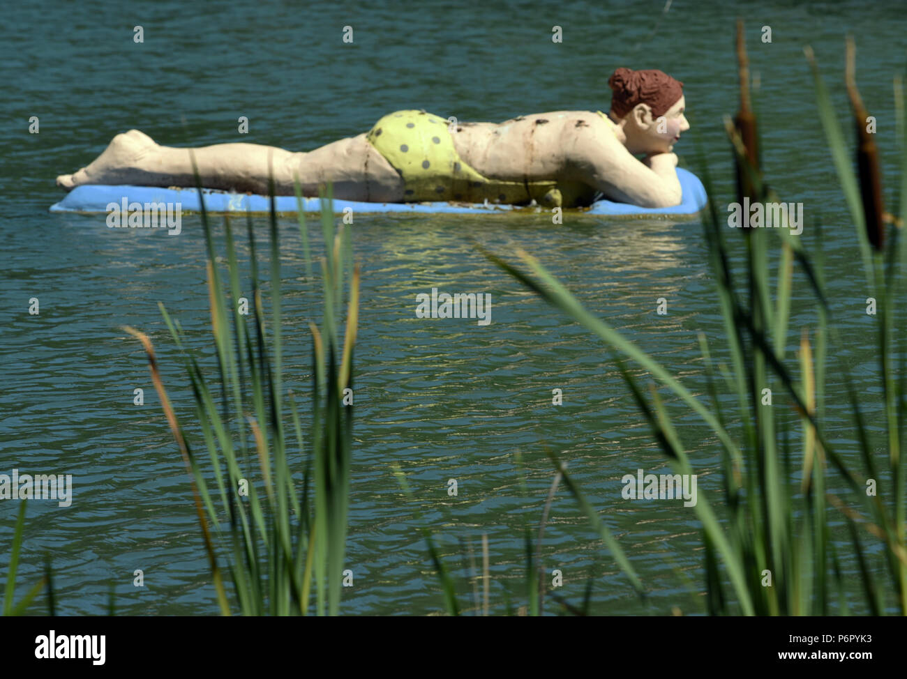 EXKLUSIV - 30.06.2018, Nordrhein-Westfalen, Witten: Eine Figur, ein sogenannter "alltagsmensch", der Künstlerin Christel Lechner, eine deutsche Bildhauerin, Töpfermeisterin und Installationskünstlerin, Balatonfüred auf einer Luftmatratze in einem Teich im maxipark. Lechner entwirft lebensgroße Betonfiguren, deren Vorbild "Menschen sind, denen man täglich begegnet reale. Lechner zeigt ihre Figuren nicht im Museum, sondern im öffentlichen Raum, dort wo ihre Menschen den Alltag erleben. Noch bis zum 4. November 2018 kann man ihre "Alltagsmenschen" in einer Open-Air-Ausstellung im Maxipark in Hamm erleben. Stockfoto