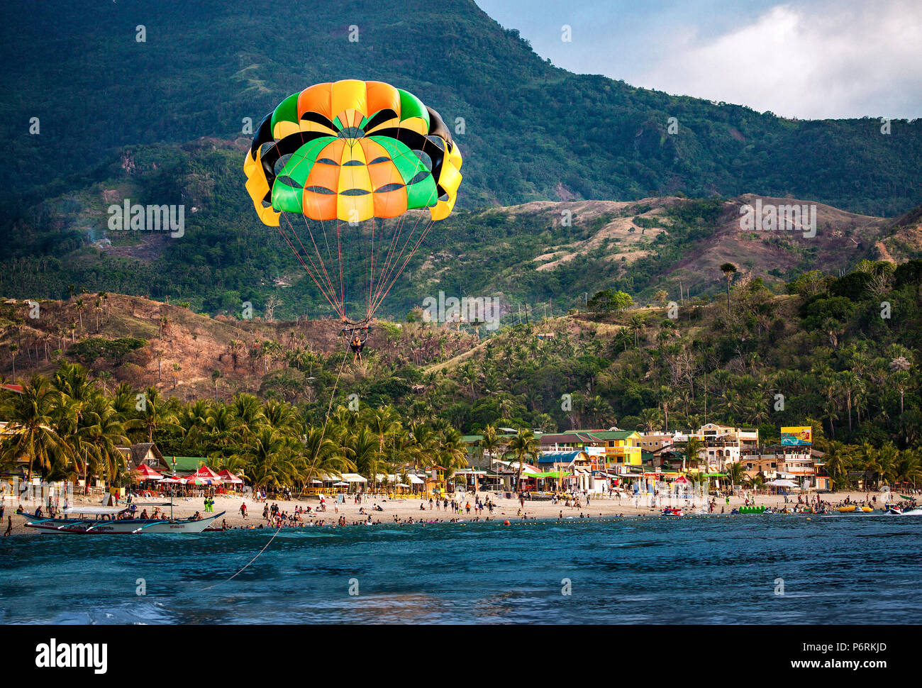 Parasailing über Weißen Strand gefüllt mit Hunderten von Menschen im Urlaub in Puerto Galera, Oriental Mindoro, Philippinen. Stockfoto