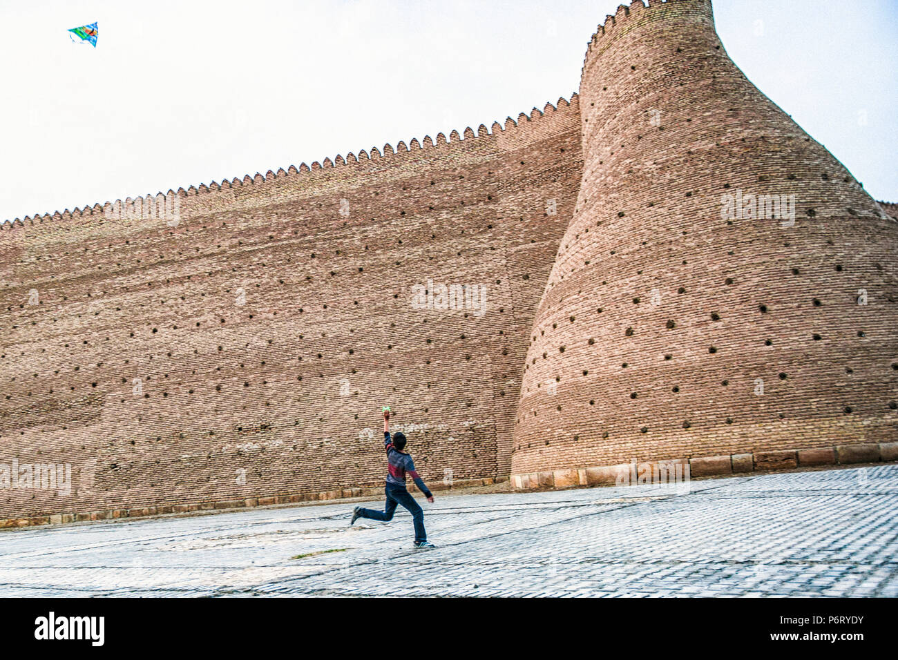 Ein Junge läuft, seine Drachen Fliegen an der Wand entlang der Bundeslade Buchara, Usbekistan Stockfoto