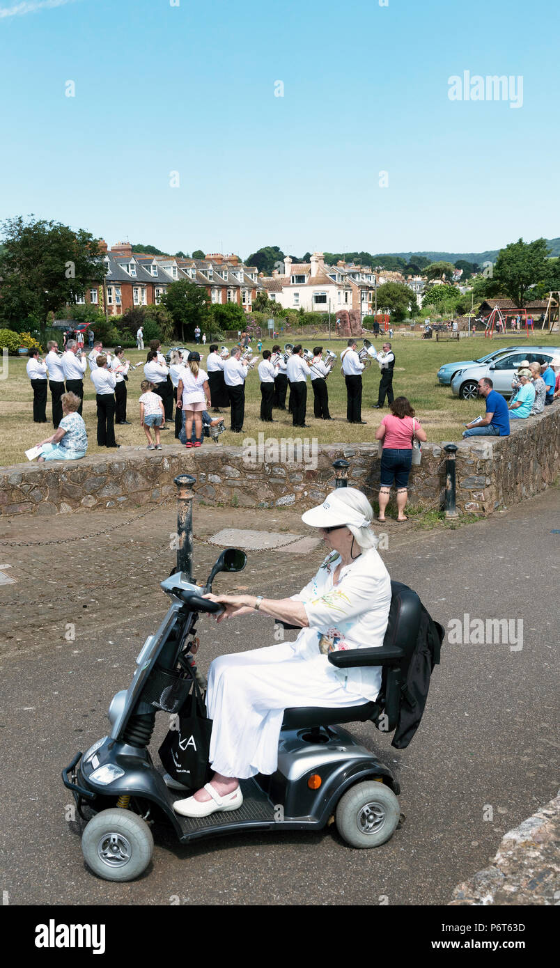 Sidmouth East Devon, England UK. Die sidmouth Stadt Band spielen auf der Ham während eines bewaffneten Kräfte Tag in Sidmouth. Frau reiten ein Mobility Scooter Stockfoto