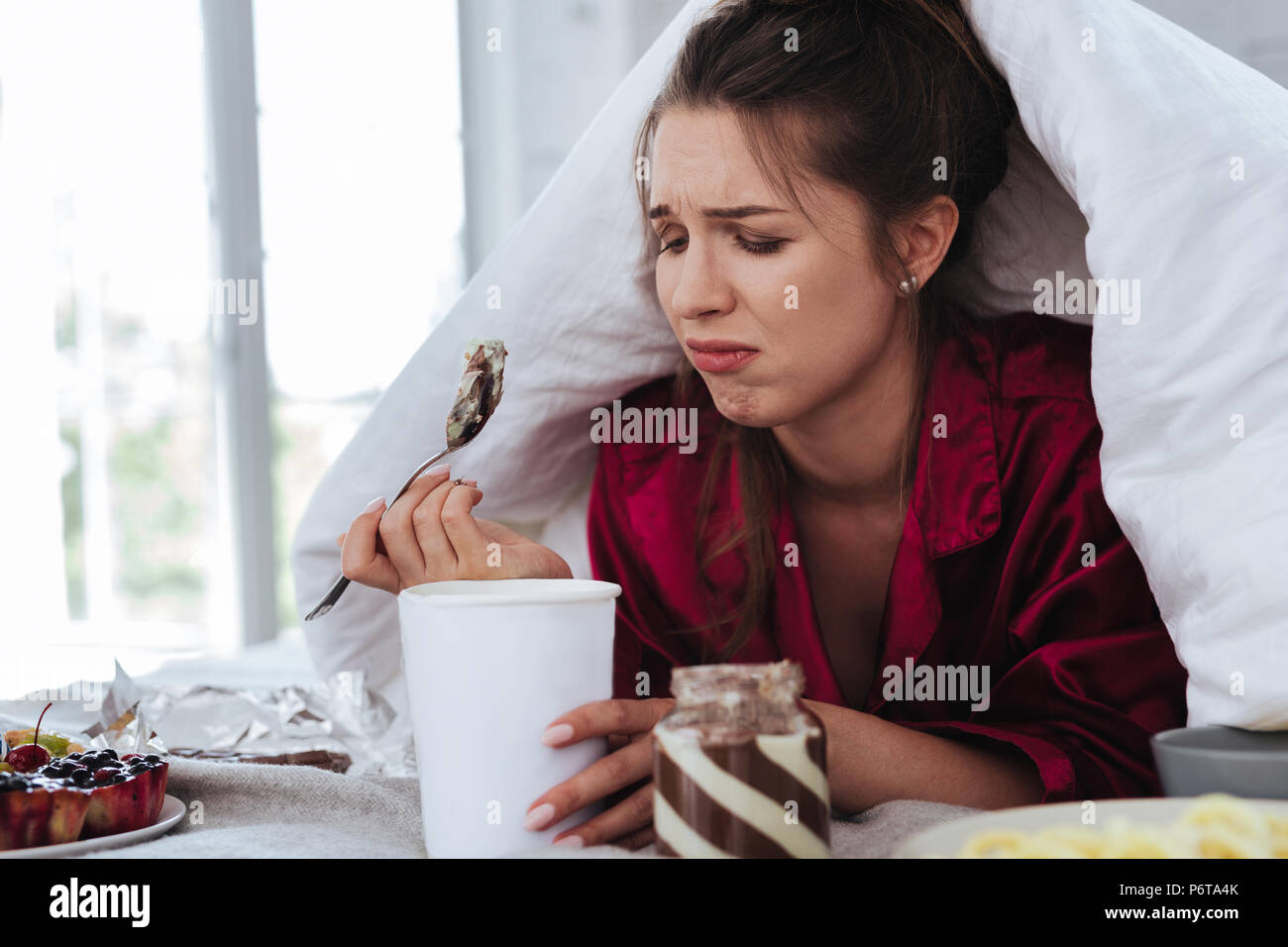 Betonte Frau versteckt unter Bettdecke Eis essen Stockfoto