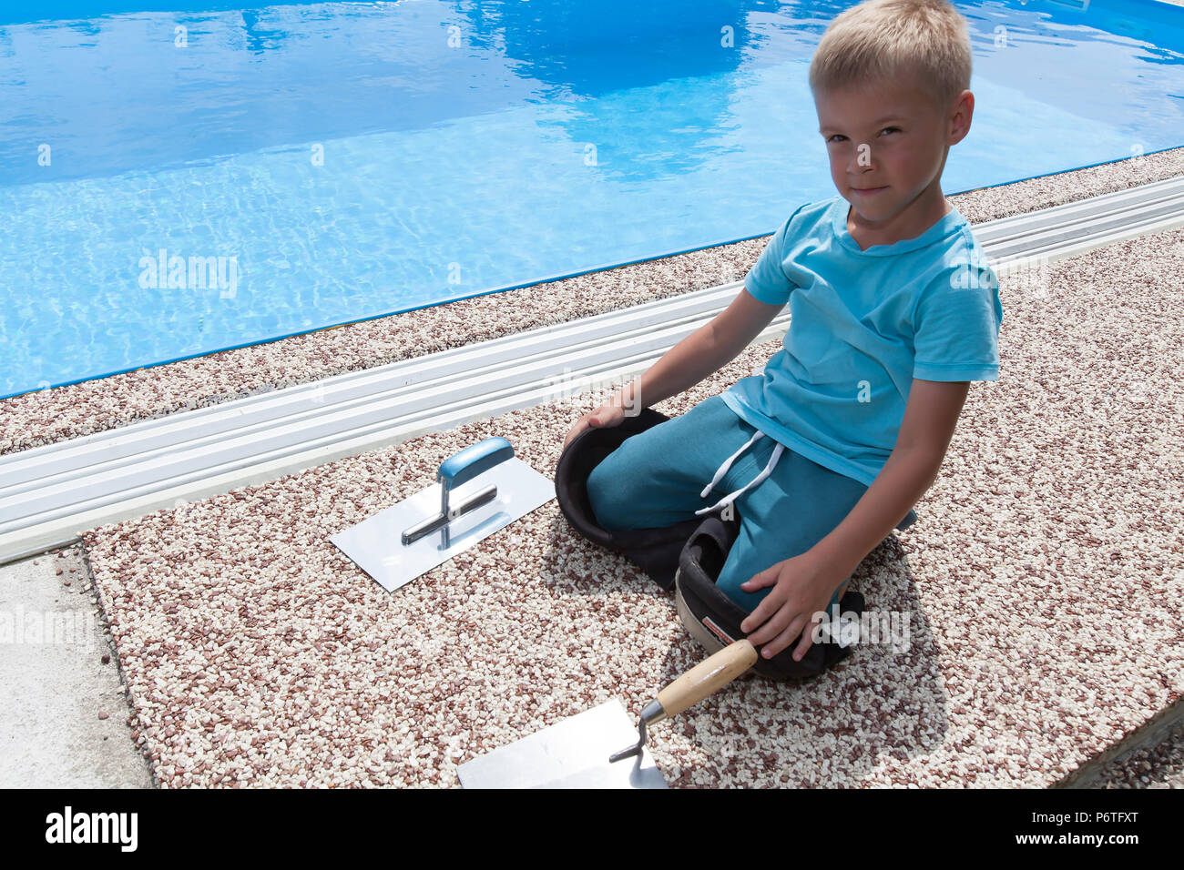 Ein kleiner Junge arbeitet an einer neuen Pflaster um den Pool herum. Stockfoto