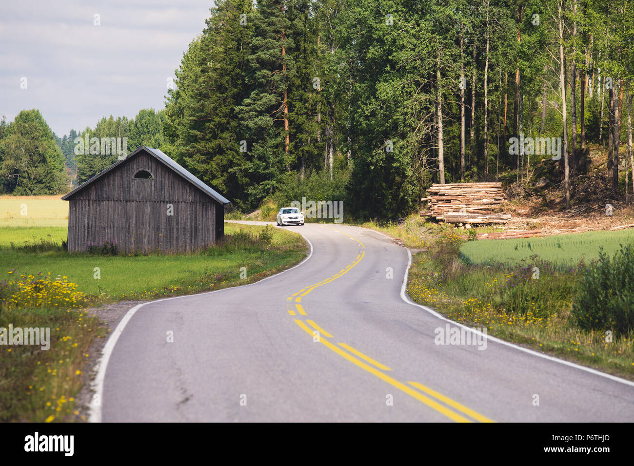 Weißes Auto fahren alte asphaltierte Straße in Landschaft und vorbei an alten Scheune und Flor auf sonnigen Sommertag anmelden Stockfoto