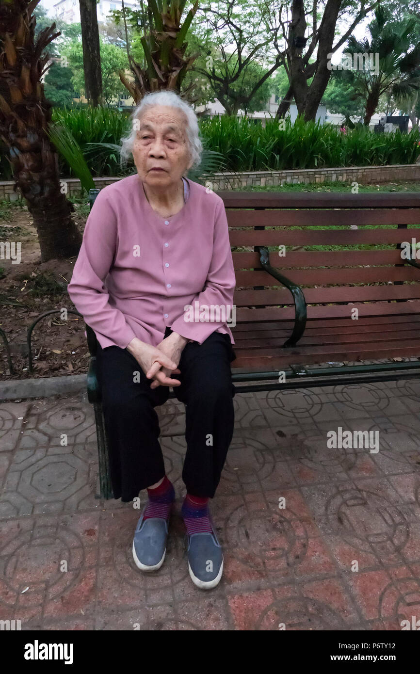 Ältere Frau allein auf einer Bank sitzen, die über den legendären See Hoan Kiem, Hanoi, Vietnam auf der Suche Stockfoto