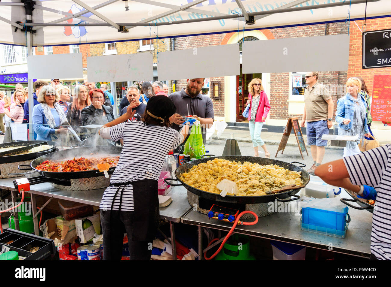 Frau übergabe Lebensmittel über auf Französisch warmes Essen im Freien Markt zu Mann im Stall. Kessel mit Paella und andere Nahrungsmittel kochen, Menschen. Stockfoto