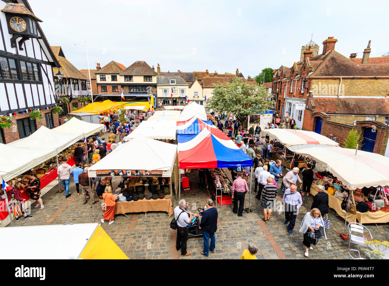 Hohen winkel Aussichtspunkt, der französische Markt von Le Wochenende Veranstaltung in Sandwich mittelalterliche Stadt, England. Vier Reihen von Ständen in der Stadt, Leute. Französische Fahnen Stockfoto