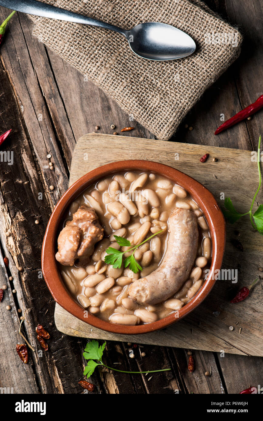 High-Angle Shot eines Steingut Schale mit einem Cassoulet de Castelnaudary, eine typische Bohneneintopf von Occitanie, in Frankreich, auf einem rustikalen Holztisch Stockfoto