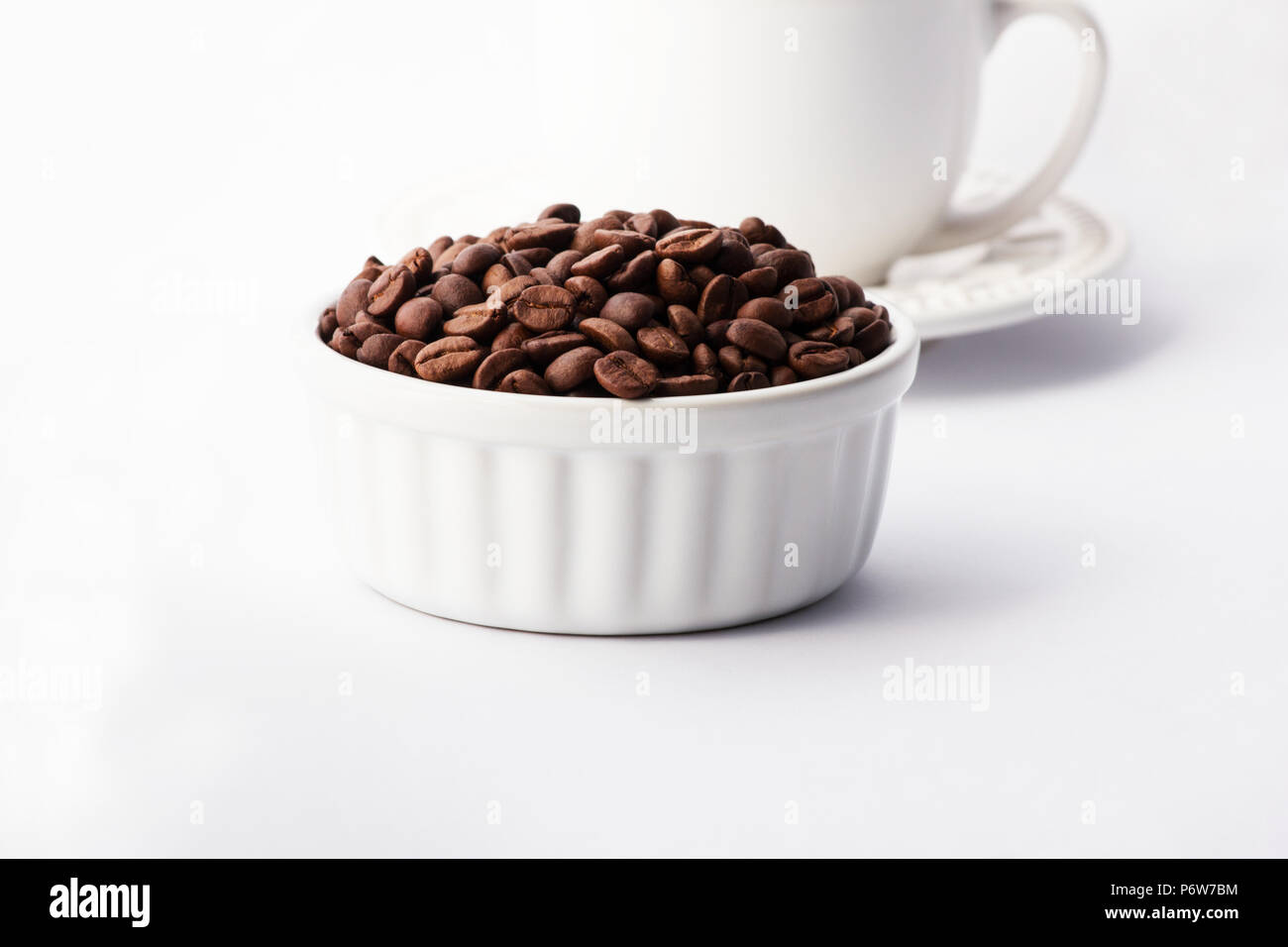 Kaffeebohnen in einer weißen Schüssel mit einer Tasse Kaffee auf weißem Hintergrund Stockfoto
