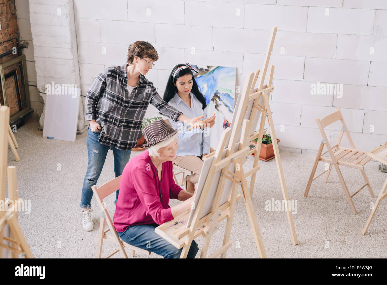 Hohen winkel Portrait von Studenten Malerei sitzt von staffeleien in art studio mit weiblichen kunst Lehrer geben Kommentare zu junge Frau in der Klasse, kopieren Raum Stockfoto