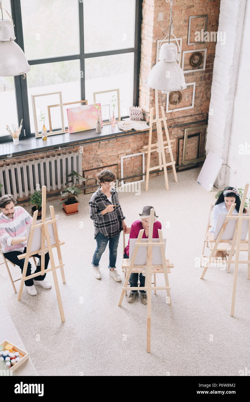 Oben Ansicht Portrait von Studenten Malerei sitzt von staffeleien in art studio mit weiblichen kunst Lehrer beobachten Sie in geräumigen und lichtdurchfluteten Dachboden, Kopieren s Stockfoto