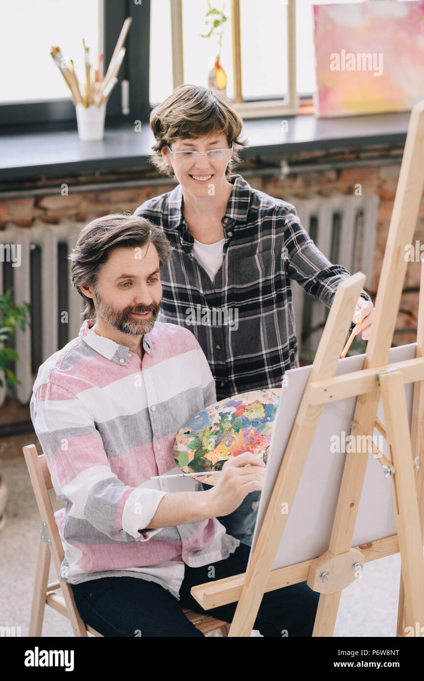 Hohen winkel Portrait von erwachsenen Schüler Gemälde von staffelei sitzen in art studio mit weiblichen kunst Lehrer ihn in der Kunst der Klasse, kopieren Raum Stockfoto