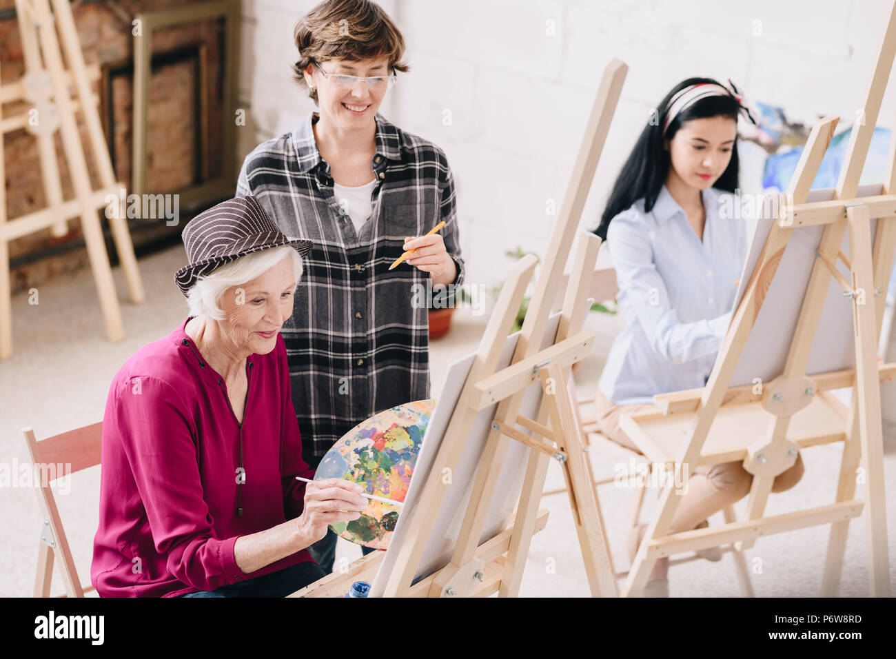 Portrait von eleganten Senior Frau Malerei an der Staffelei im Atelier mit lächelnden Lehrerin, Kommentare, Kopie Raum Stockfoto