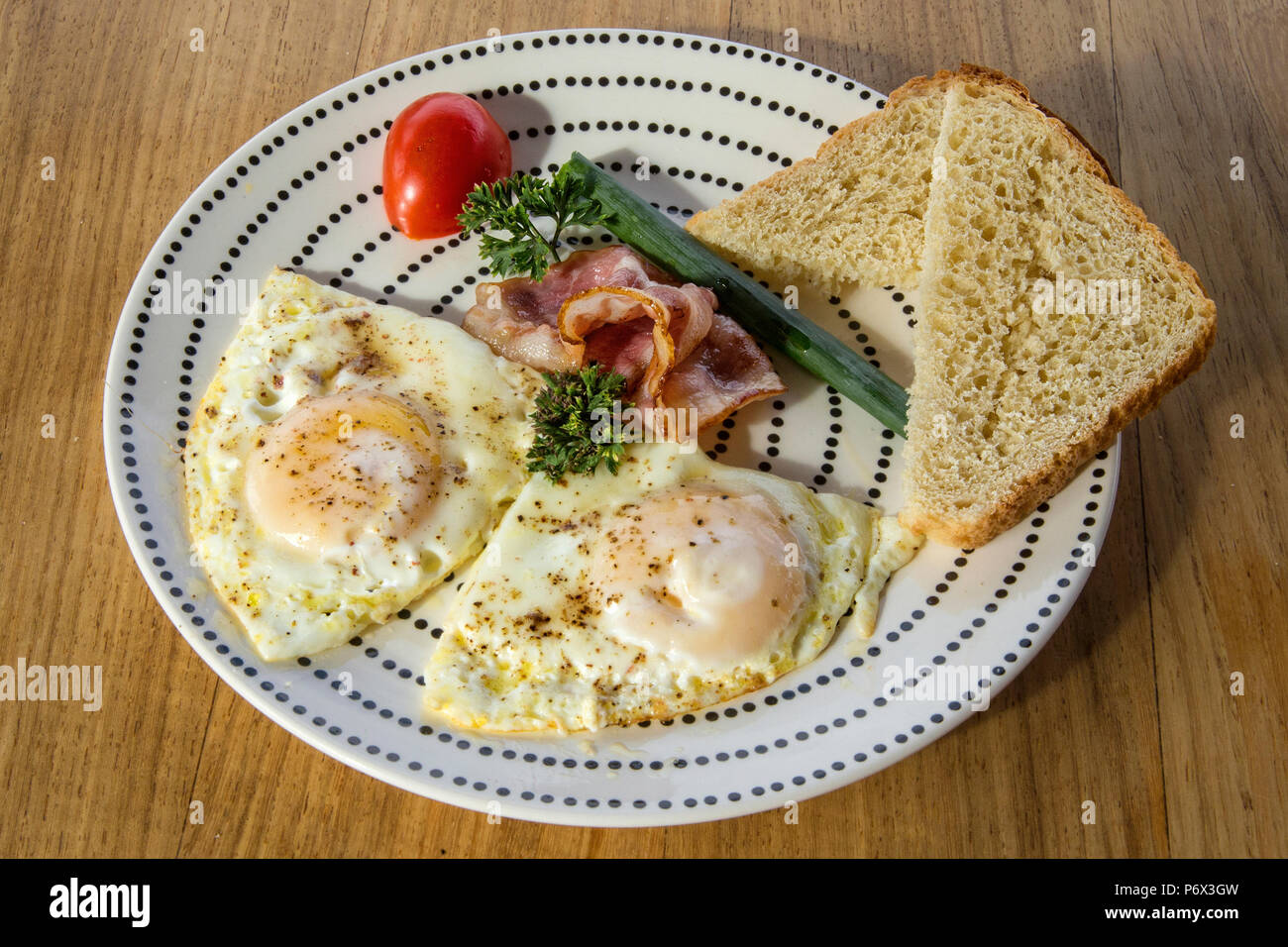 Eier, Schinken und Tomaten, garniert und auf einem Teller mit Brot auf die Seite legen Stockfoto