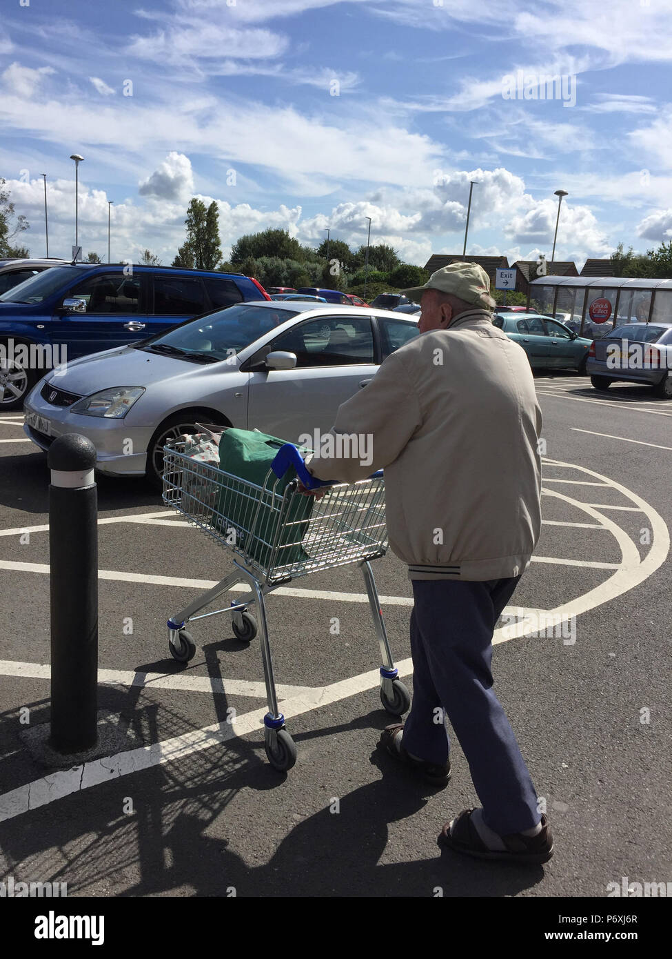 Ansicht der Rückseite des älteren Mannes schieben Einkaufswagen im Supermarkt Parkplatz Stockfoto