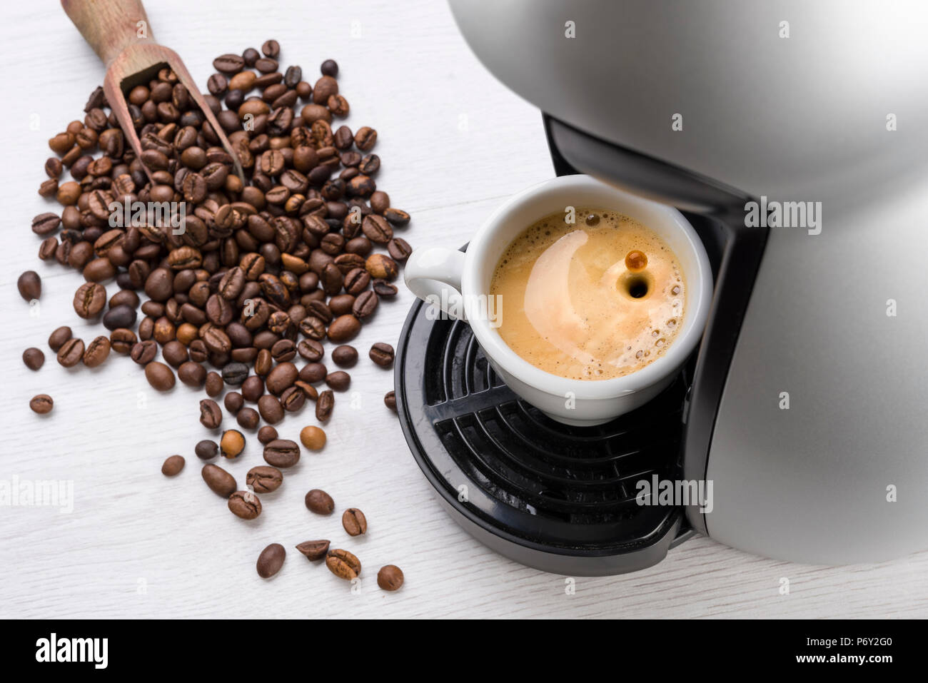 Tasse Kaffee nur gefüllt auf der Maschine mit Drop springen und Kaffeebohnen auf Tisch Stockfoto