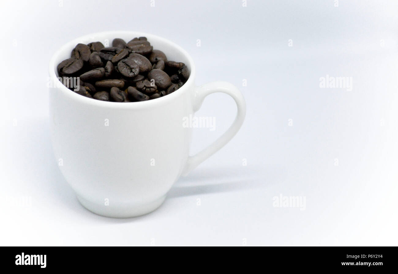 Eine Espresso-Tasse gefüllt mit gerösteten Kaffeebohnen. Das Bild ist linksbündig ausgerichtet und verfügt über verfügbaren Kopierspeicher Stockfoto