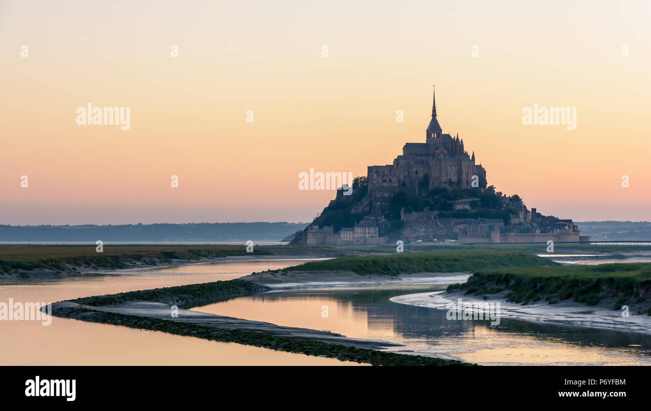 Der Mont Saint-Michel in der Normandie, Frankreich, bei Sonnenaufgang und Flut mit den warmen Farben des Himmels spiegelt sich in den Gewässern des Couesnon. Stockfoto