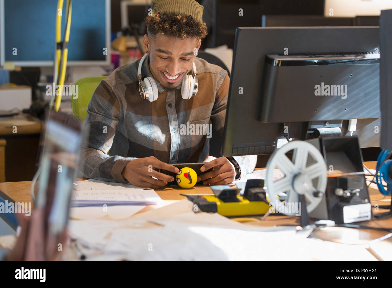 Lächelnde kreative Geschäftsmann mit Kopfhörern über Smart Phone am Computer im Büro Stockfoto