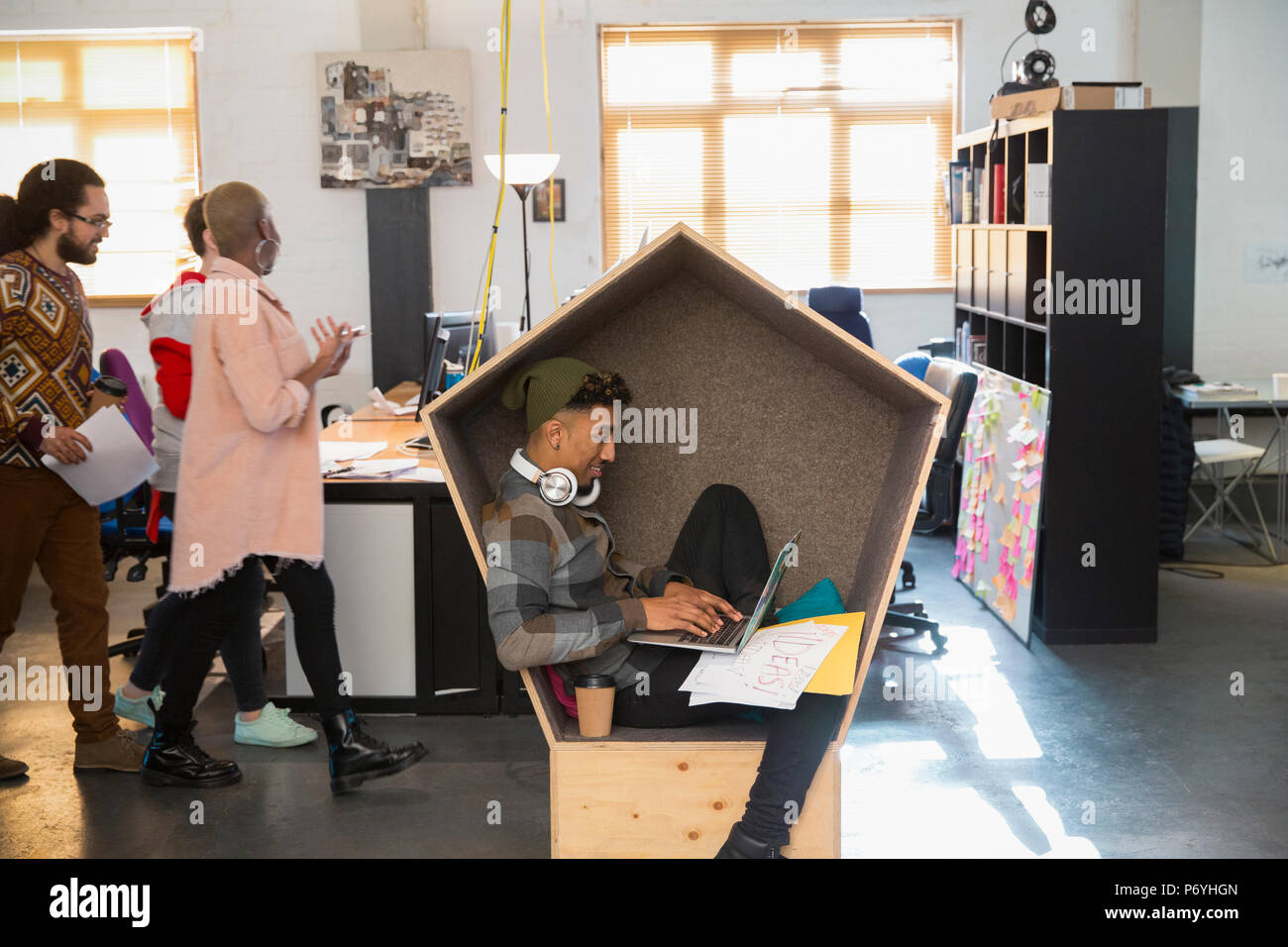 Kreative Geschäftsmann mit Kopfhörern am Laptop arbeiten in cubby Stockfoto