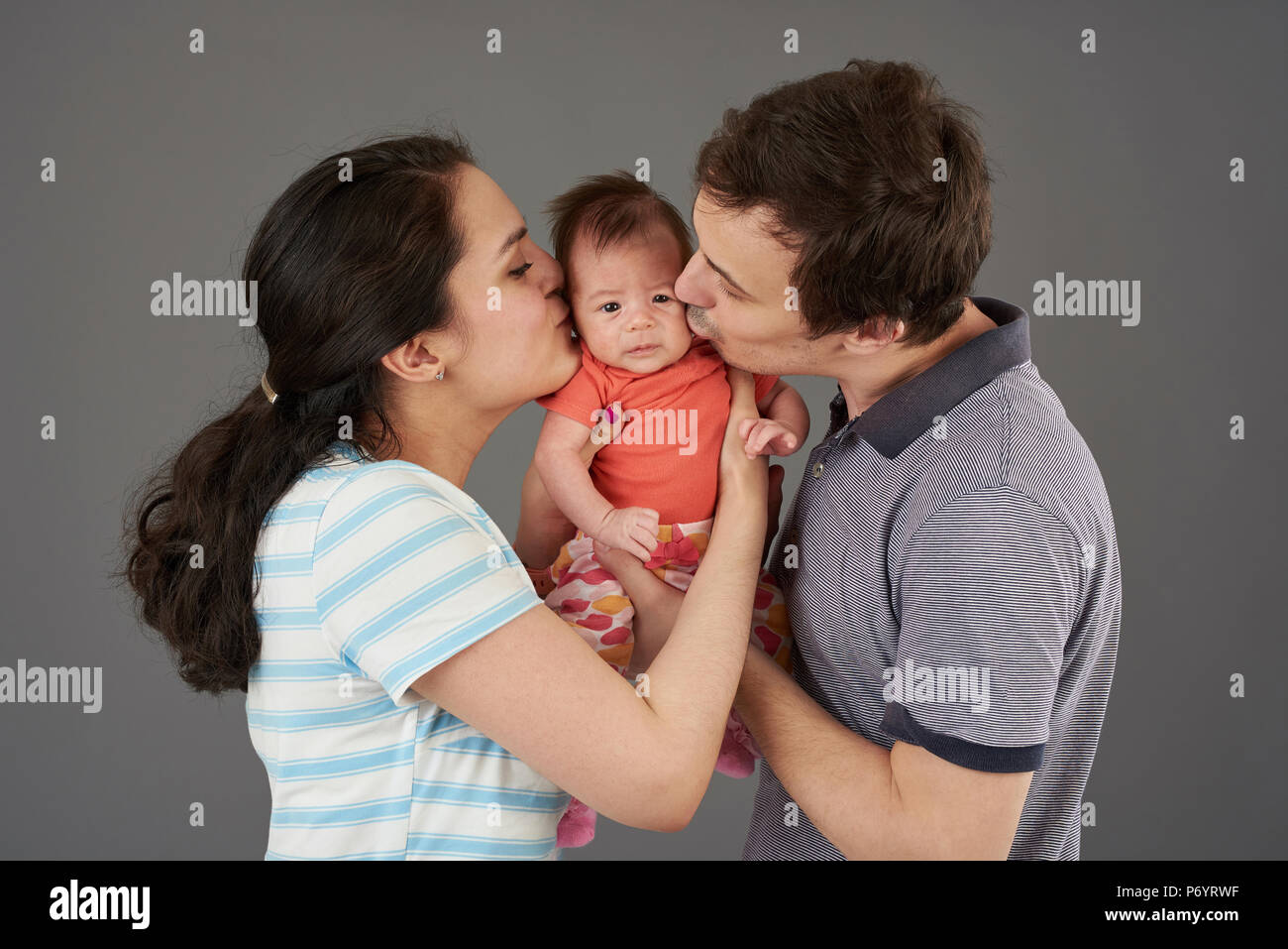 Junge Eltern Kuss kleines Baby Mädchen auf grauem Hintergrund Stockfoto