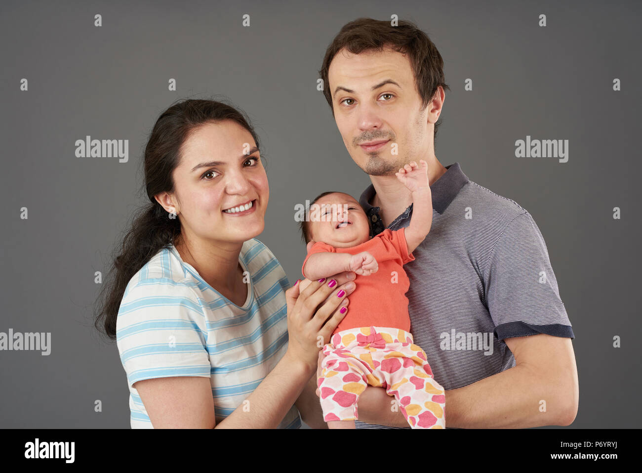 Junge Eltern mit kleinen Babys auf grauem Hintergrund Stockfoto