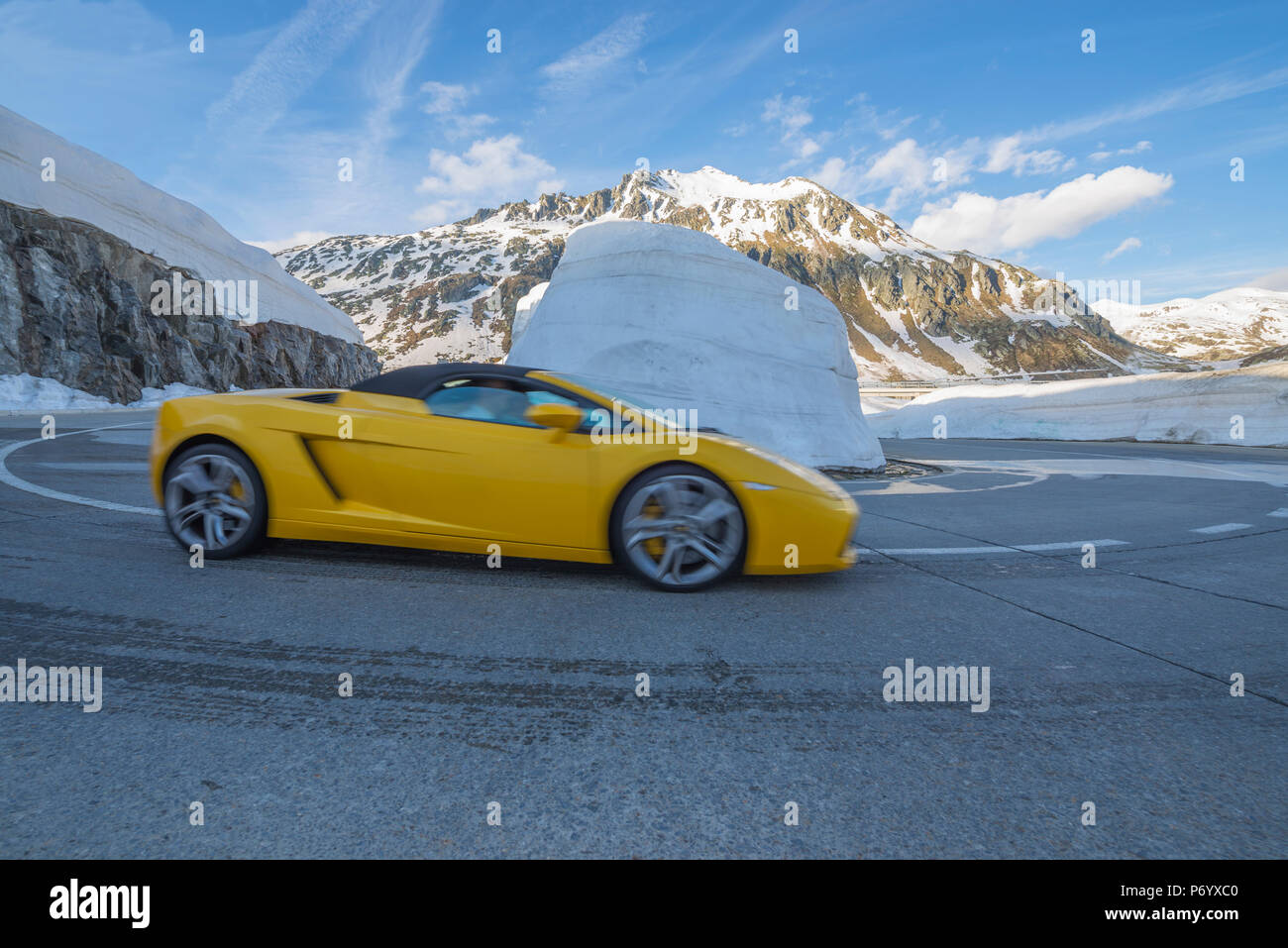 Gelber Lamborghini Auto in eine Haarnadelkurve mit Schnee und die  schneebedeckten Berge im Hintergrund und blauen Himmel mit Wolken in der  Schweiz Stockfotografie - Alamy