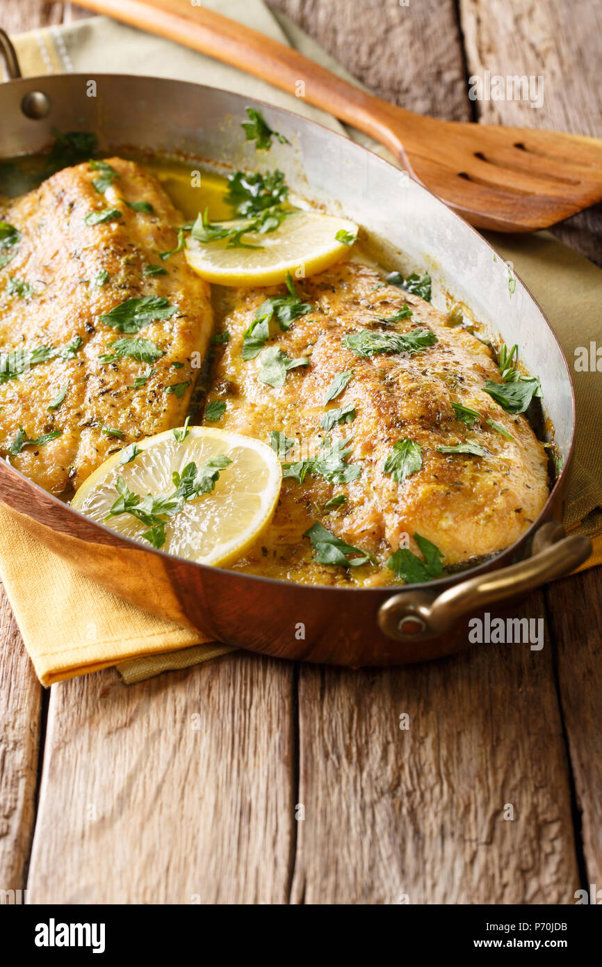 Traditionelle mediterrane essen: gebackene Forelle mit Knoblauch Butter, Zitrone und Petersilie close-up in einem Kupfer Pfanne auf dem Tisch. Vertikale Stockfoto