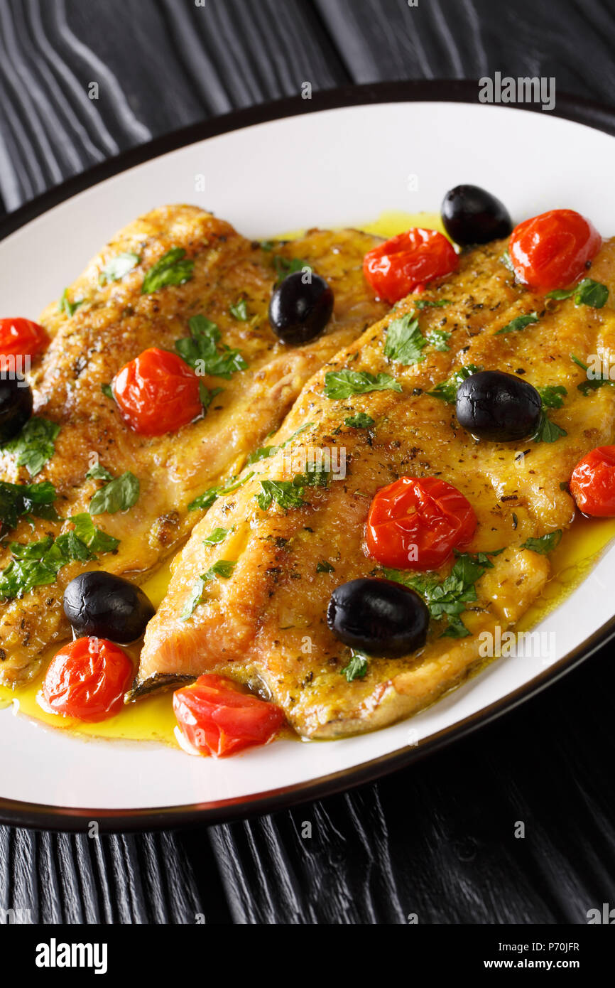 Forellen Rezept mit Knoblauch Zitrone Butter Kräutersoße Tomaten und Oliven closeup auf einem Teller. Vertikale Stockfoto